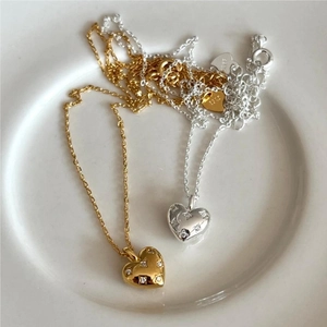 Detail of silver and gold heart necklaces with zircon inlay on a ceramic plate