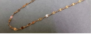 Dettaglio di una catena a labbro dorata su velluto grigio con maglie lisce e lucide