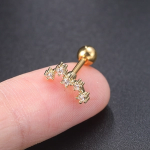 Detailed macro view showing a gold-plated curved ear stud with five inlaid zircons on a finger