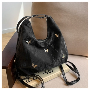 Detail of black pleated fabric bag with butterfly hardware on a beige chair