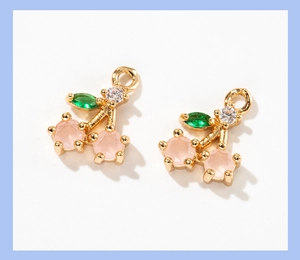 Detail of cherry jewelry pendants with pink crystals and green leaf stones on gold base