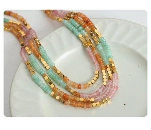 Detail of beaded necklace with colorful amazonite and gold beads on a ceramic plate