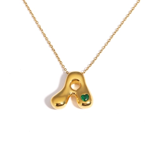Detail of 18k gold plated bubble letter A necklace with a green heart gemstone