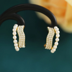 Detail of elegant gold-tone pearl and rhinestone double hoop earrings on dark green background
