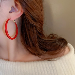 Close-up of large red glossy hoop earring worn by a model in warm natural light