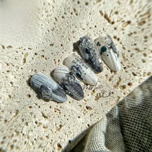 Macro detail of plaid nail stickers with ink art and faux pearls on beige stone