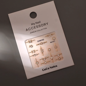 Close-up of gold nail charms and rhinestones on MJ-011 display card on grey background