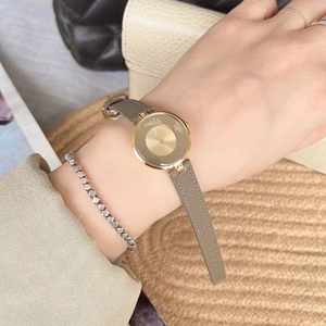 Minimalist women's gold round watch with grey leather strap styled on a model's wrist