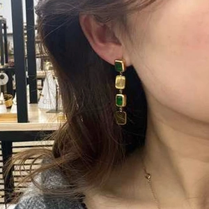 Detail of long gold drop earrings featuring green square gems on a female model