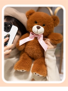 Close-up of a soft brown teddy bear plush with a pink polka dot bow held by a model