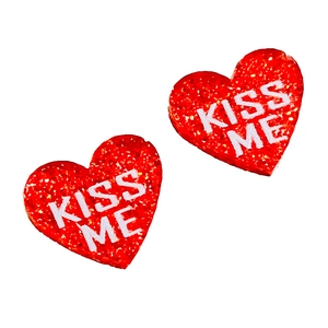 Détail de boucles d'oreilles cœur rouge pailleté avec texte KISS ME sur fond blanc