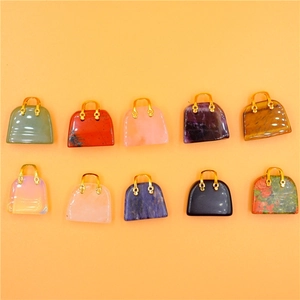 Close-up of ten colorful crystal handbag pendants with gold handles on orange background