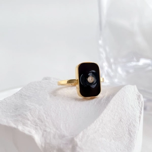 Detailed view of a gold square ring with black enamel inlay and a centered diamond accent