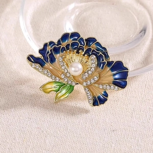 Close-up of golden floral brooch with enamel petals, white pearl and sparkling rhinestones