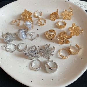 Flat lay of gold and silver irregular floral rings with pearls on a ceramic tray