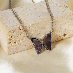 Macro shot of purple zircon butterfly pendant on silver chain over champagne silk fabric