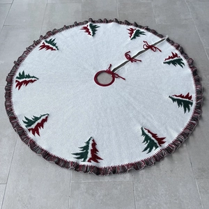 Detail of white knitted Christmas tree skirt featuring red green trees and fringe trim