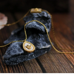 Detailed view of crown-engraved drop shell pendant on 18K gold-plated bead chain