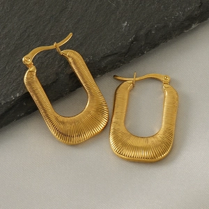 Detail view of gold U-shaped earrings with radial texture on a silk and stone background