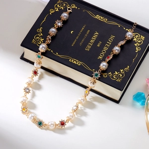 Golden necklace with white pearls and colorful gems on a vintage black notebook