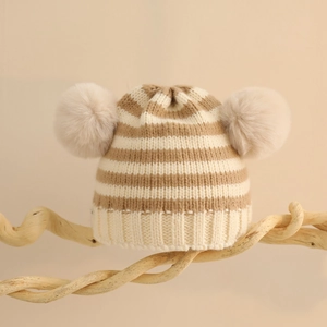 Dettaglio del berretto in maglia a righe per neonati con due grandi pompon in eco-pelliccia