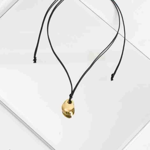 Detail of a golden bean pendant with smooth metallic finish on a black cord necklace