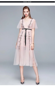 Détail d'une robe en tulle rose avec broderies florales et fine ceinture noire à la taille