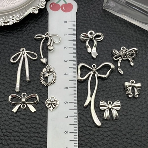 Silver bow and heart alloy charms set for DIY jewelry making displayed with ruler