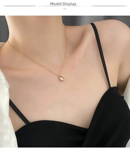 Close-up of a natural pink pearl pendant necklace on a gold chain worn by a female model