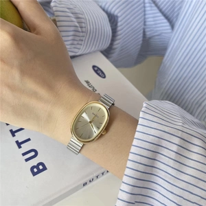 Close-up of a ladies' oval gold-tone watch with silver link band on a wrist