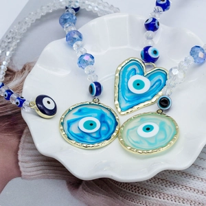 Close-up of blue Evil Eye heart charms and crystal beads in a white shell dish