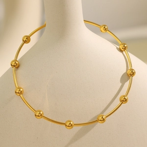Minimalist golden bead bracelet displayed on a white textured ceramic vase neck
