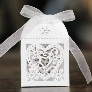 Detail of white laser-cut heart candy box with elegant floral patterns and organza ribbon