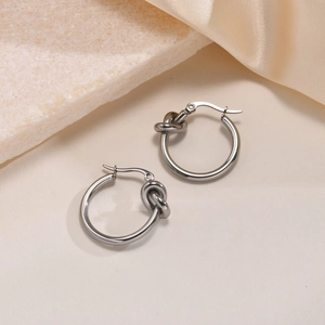Polished silver knot hoop earrings made of stainless steel on silk background