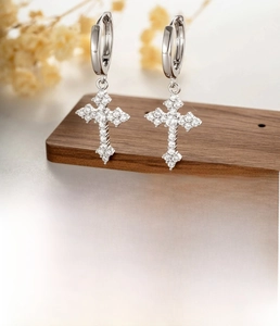 Macro detail of silver cross earrings with zircon pavé setting on a wood texture