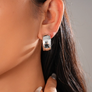 Macro shot of a silver polished C-shaped earring worn on ear showing reflective finish