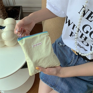 Close-up of a small pale yellow pleated nylon makeup bag with a sky blue zipper puller
