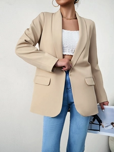 Détail d'un blazer beige long avec poches à rabat porté avec un jean en denim bleu
