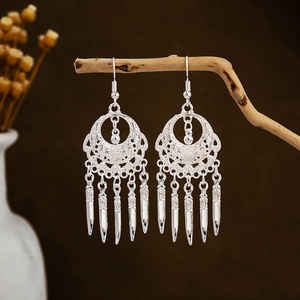 Detailed view of silver ethnic leaf tassel earrings hanging on a natural wooden branch