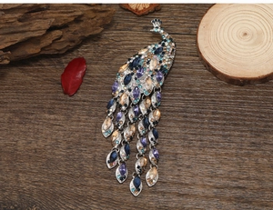 Close-up of peacock brooch with colorful rhinestones and tassels on a dark wood base