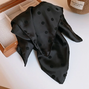 Dettaglio di sciarpa in seta nera a pois drappeggiata su tavolo con decoro vintage