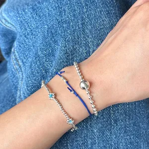 Detail shot of three-piece silver bead and blue floral charm bracelets on wrist