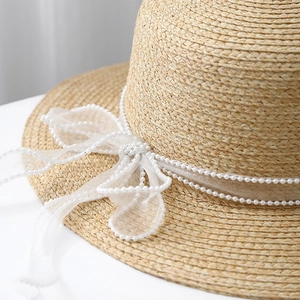 Macro detail of beige straw sun hat featuring elegant organza ribbon and pearl trim