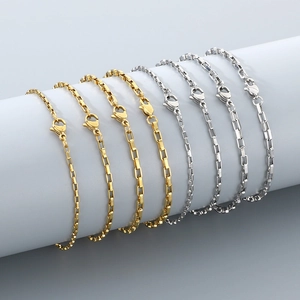 Golden and silver stainless steel box chain bracelets with lobster clasps on grey stand