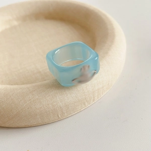 Detailed view of square blue resin ring with golden saturn orb emblem on a tray