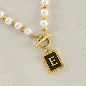 Detail of pearl necklace with gold toggle clasp and rectangular letter E pendant