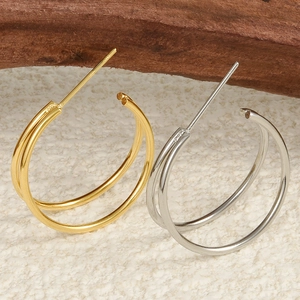 Macro shot of gold and silver double-hoop stainless steel earrings on a beige surface