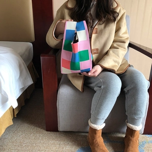Knitted tote bag with colorful checkerboard pattern held by a model in a cozy indoor setting