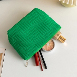 Detail of green knit cosmetic bag with silver zipper holding brushes and makeup