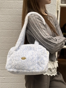 Détail d'un sac à bandoulière en peluche bleu clair avec plaque de logo dorée élégante